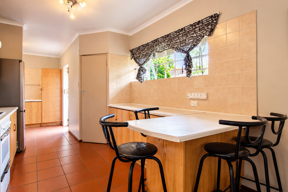 A functional kitchen featuring wooden cabinetry, tiled backsplash, ceramic flooring, and a built-in breakfast counter, offering a practical layout for daily meal preparation.