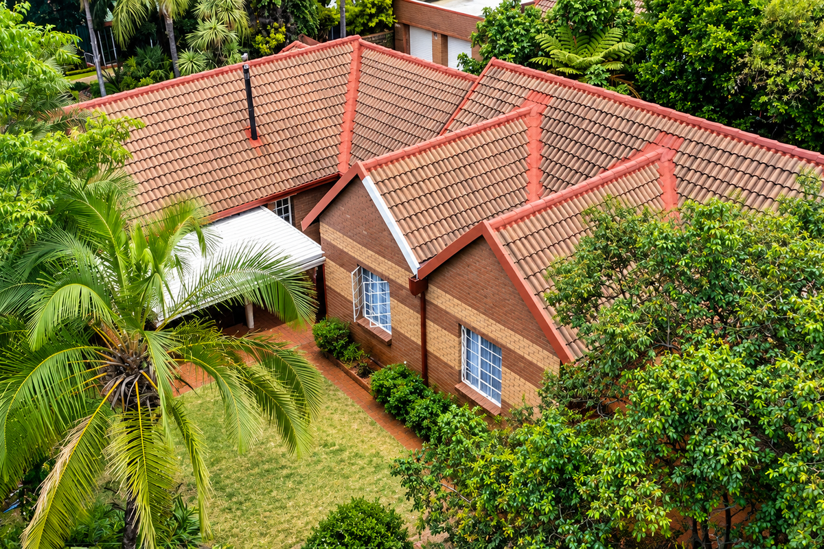Aerial view of a townhouse featuring a classic tiled roof, brick exterior, and a private garden area with mature trees.