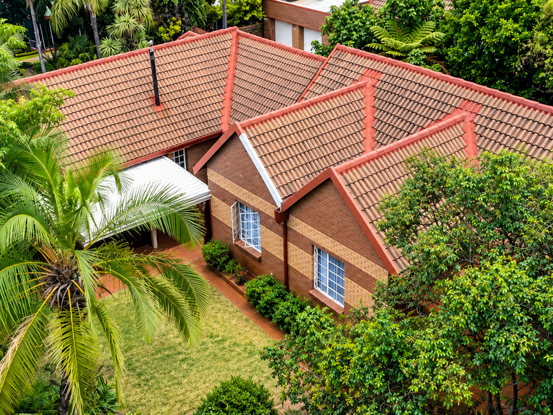 Aerial view of a townhouse featuring a classic tiled roof, brick exterior, and a private garden area with mature trees.