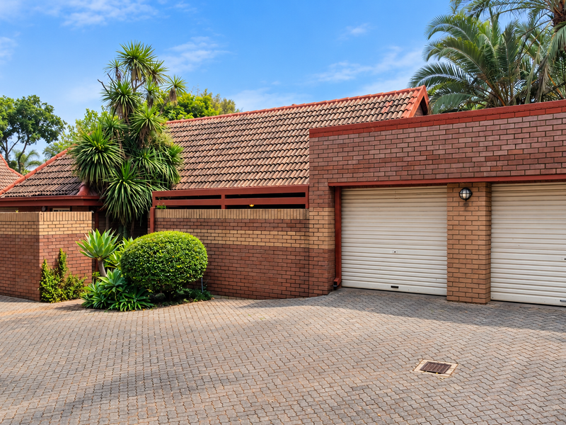 Front view of a townhouse featuring a double garage with roller shutter doors, brick facade, and a paved driveway.