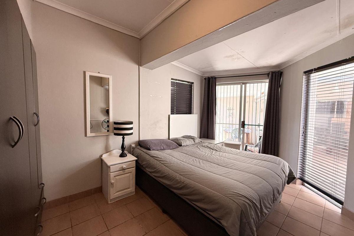A bedroom featuring tiled flooring, built-in wardrobes, and a sliding glass door with security gate providing access to the exterior.