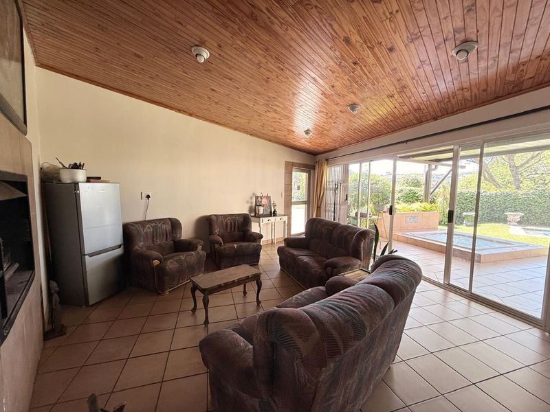 Spacious living room featuring a vaulted timber ceiling, tiled floors, and large sliding glass doors providing direct access to the patio and pool area.
