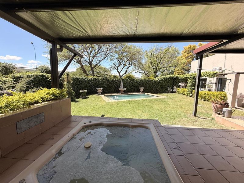 Outdoor entertainment area featuring a covered patio with a built-in jacuzzi overlooking a private swimming pool and landscaped garden.