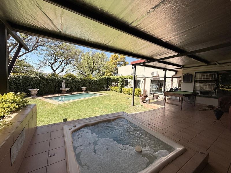 Covered patio area featuring a built-in jacuzzi, tiled flooring, and direct access to a private garden with a swimming pool.