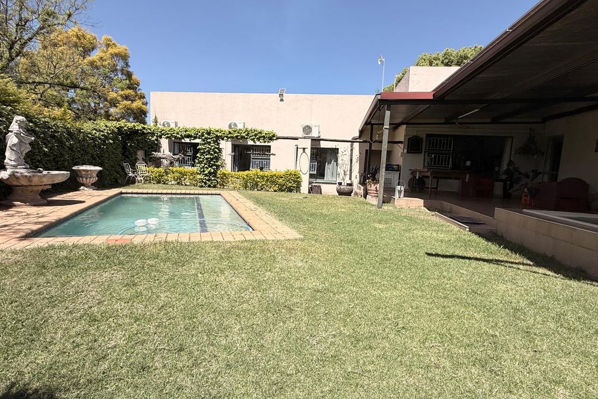 Rear garden featuring a swimming pool, a covered patio area, and established landscaping, providing a functional outdoor space for relaxation and entertainment.