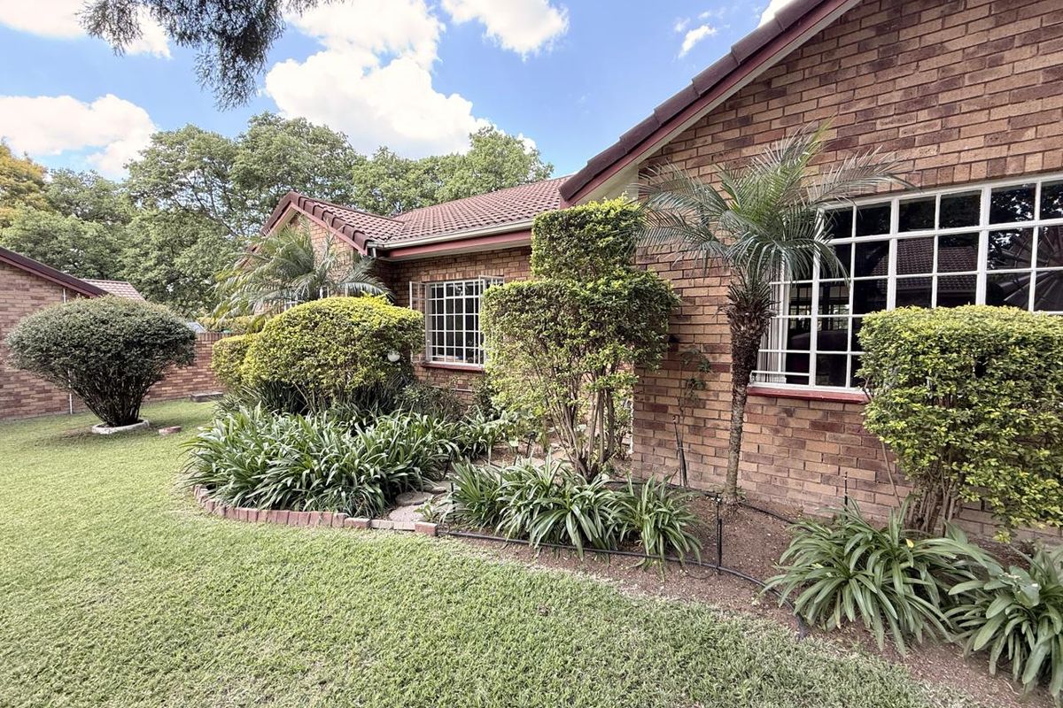 A well-maintained rear exterior view of the townhouse featuring classic face brick construction, a tiled roof, and established garden landscaping.