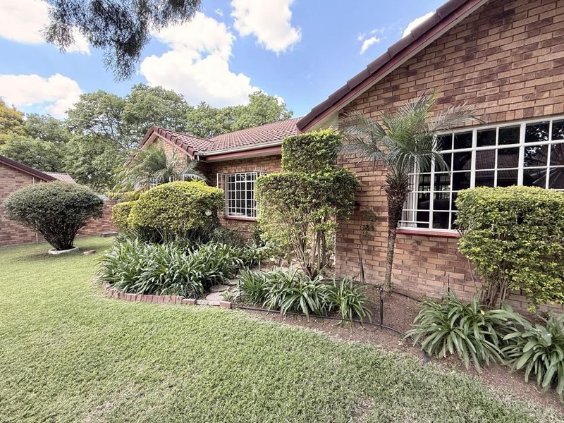 A well-maintained rear exterior view of the townhouse featuring classic face brick construction, a tiled roof, and established garden landscaping.