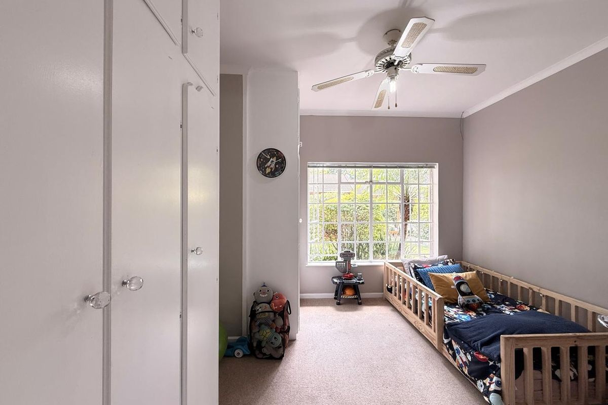 A bedroom featuring built-in cupboards, a ceiling fan, and a large grid-pattern window providing natural light.