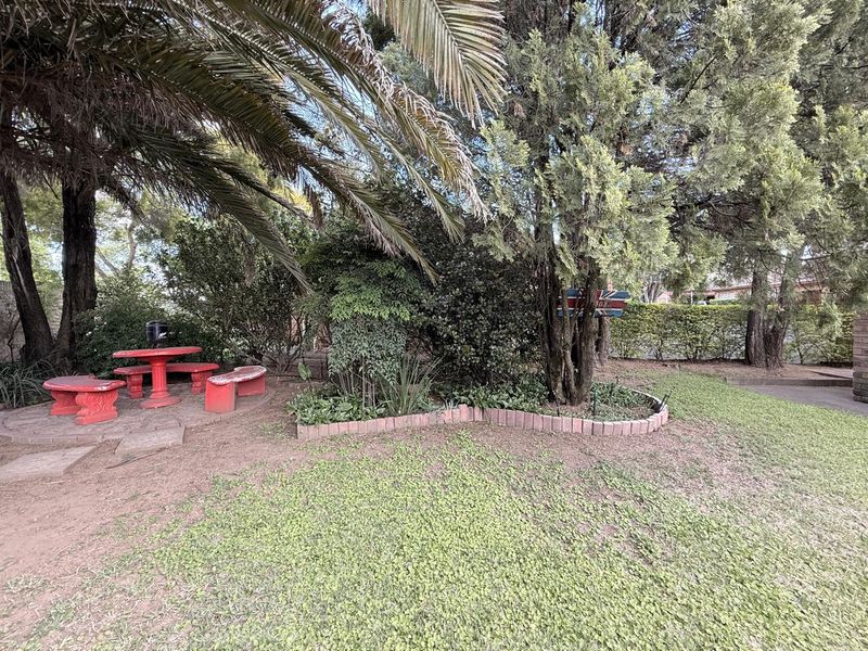 A private garden area featuring mature trees, established shrubbery, and brick-edged garden beds with a paved section.