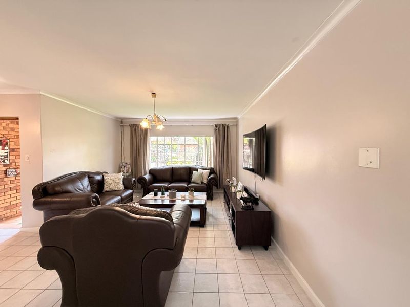 A spacious living room featuring neutral tiled flooring, coving, and a large window that provides natural light to the area.