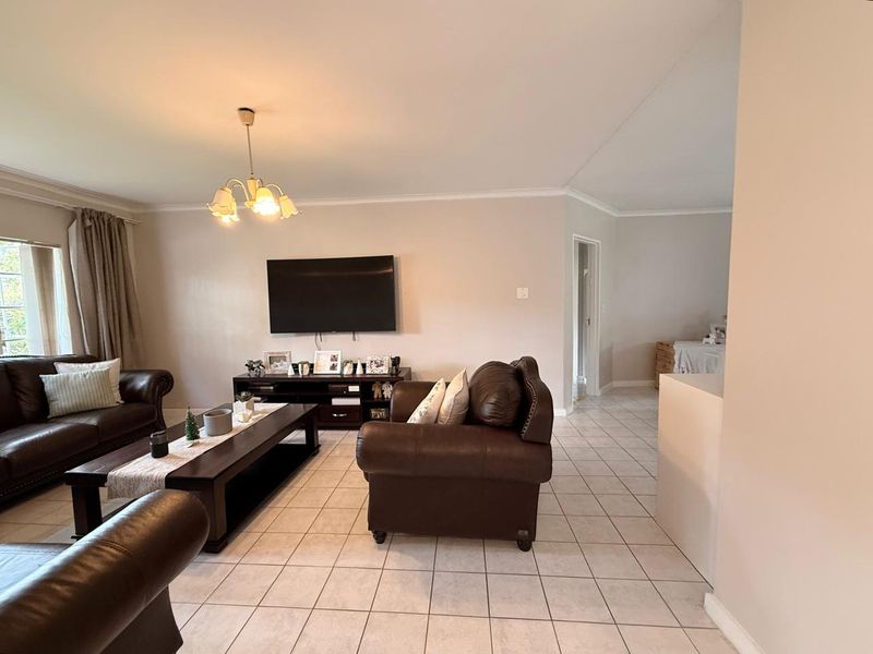 A spacious living room featuring neutral tiled flooring, coved cornicing, and a central light fixture, providing a functional and well-maintained living space.