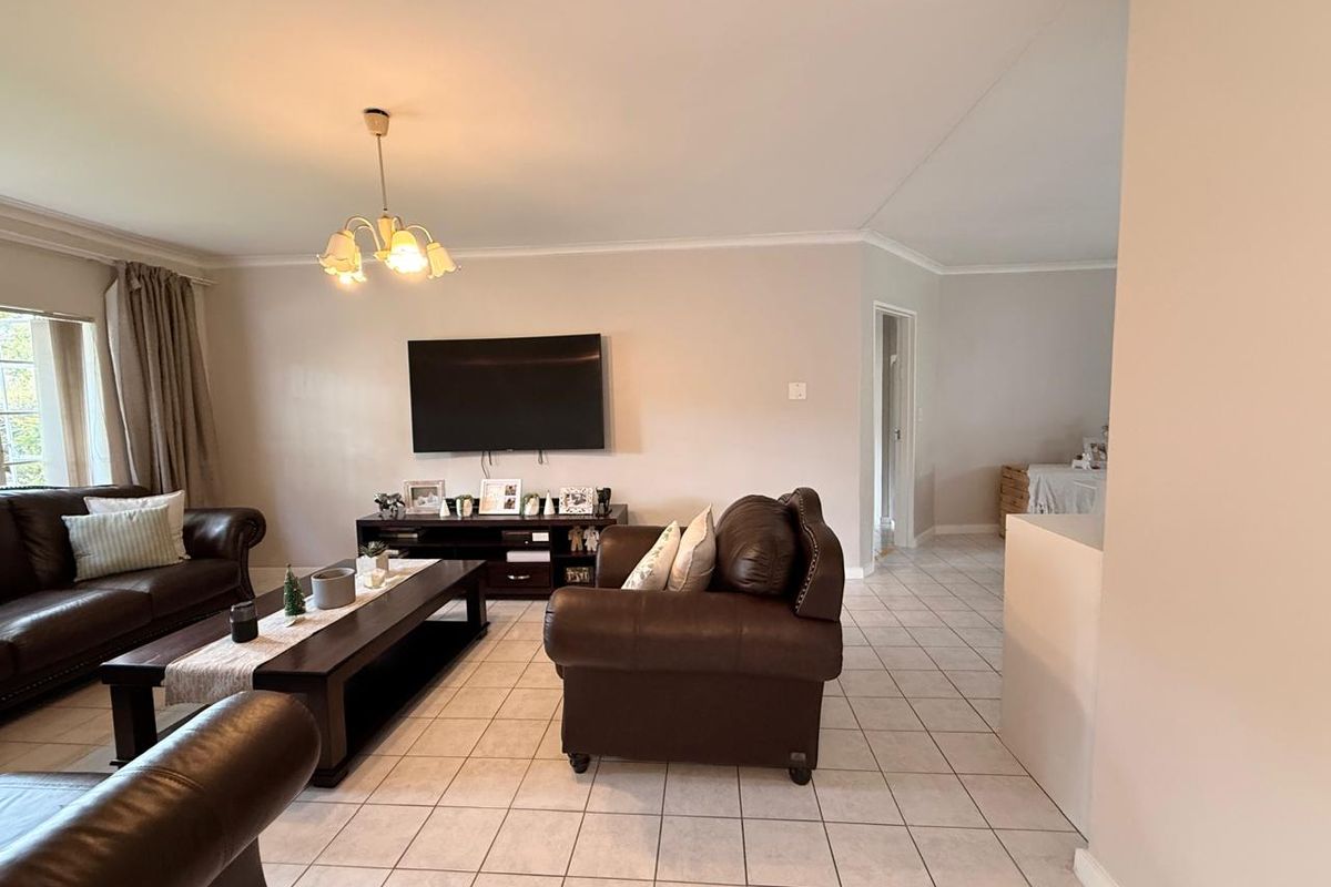 A spacious living room featuring neutral tiled flooring, coved cornicing, and a central light fixture, providing a functional and well-maintained living space.