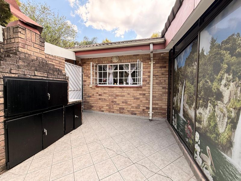 A private outdoor patio area featuring a built-in brick braai, tiled flooring, and direct access to the interior through large sliding glass doors.