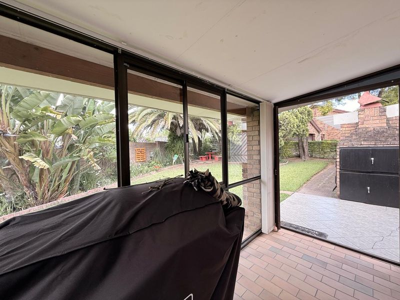Enclosed patio area featuring tiled flooring, sliding glass doors, and a built-in braai, offering direct access to the rear garden.