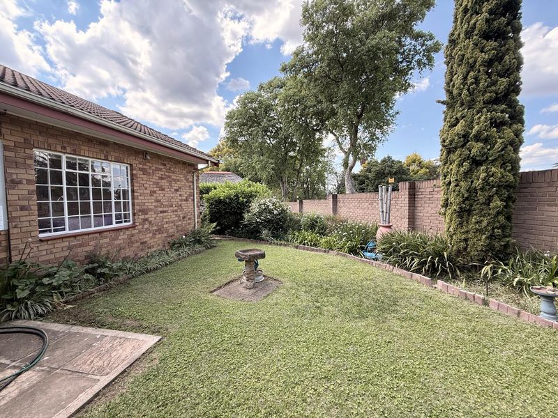 A well-maintained rear garden featuring a brick boundary wall, a small paved patio area, and established lawn and landscaping.