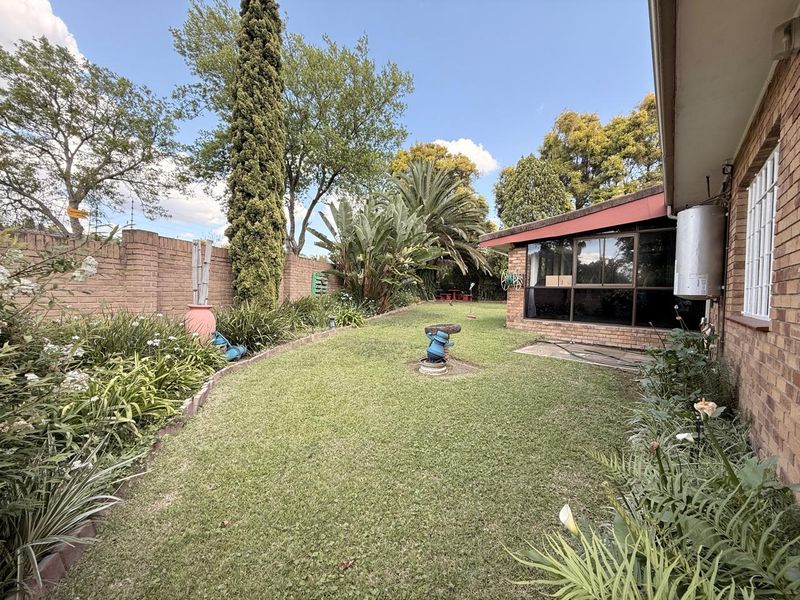 A private rear garden featuring a well-maintained lawn, established landscaping, brick boundary walls, and an external geyser mounted on the townhouse exterior.