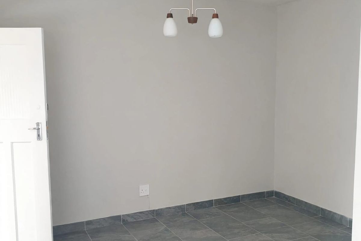 A clean, empty bedroom featuring neutral wall paint, grey tiled flooring, and a central ceiling light fixture.