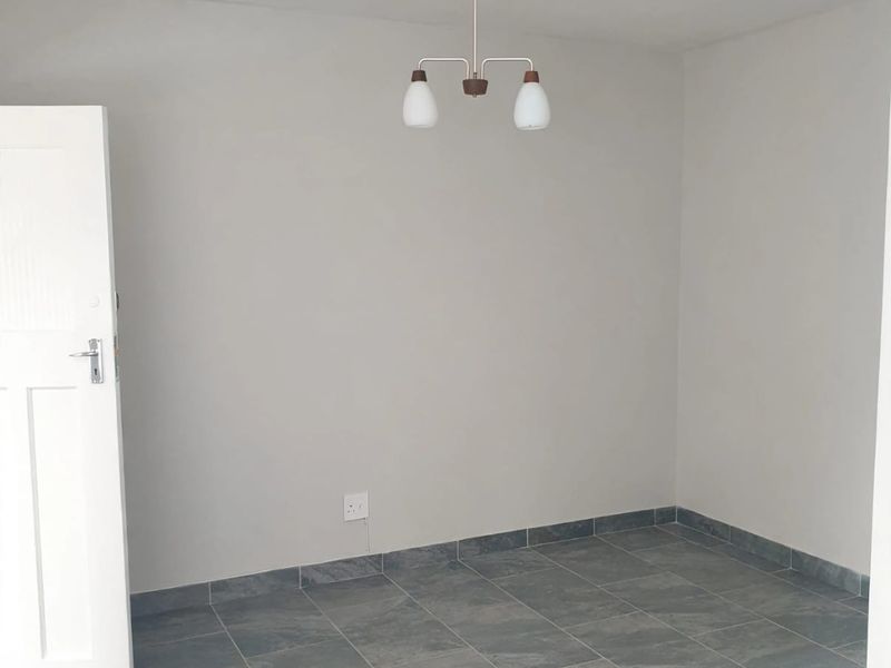 A clean, empty bedroom featuring neutral wall paint, grey tiled flooring, and a central ceiling light fixture.