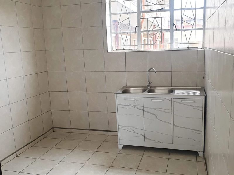 A clean, tiled scullery area featuring a double sink with a modern cabinet and a window fitted with security bars.
