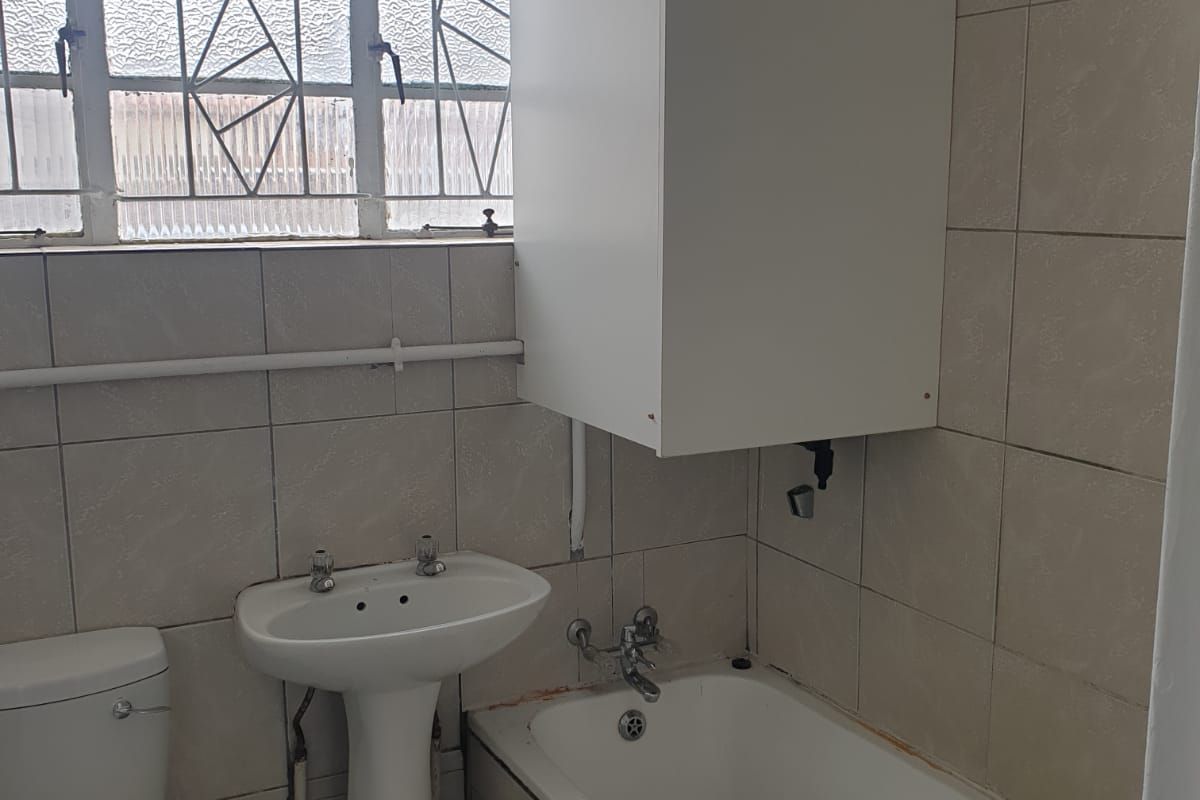 A functional bathroom featuring a pedestal basin, toilet, and bathtub with tiled finishes, requiring cosmetic updates to improve its overall condition and aesthetic appeal.