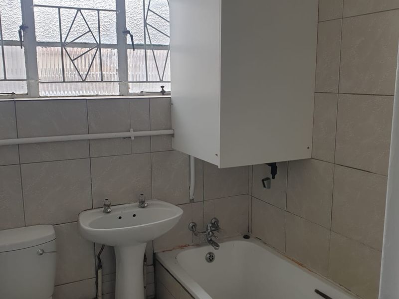 A functional bathroom featuring a pedestal basin, toilet, and bathtub with tiled finishes, requiring cosmetic updates to improve its overall condition and aesthetic appeal.