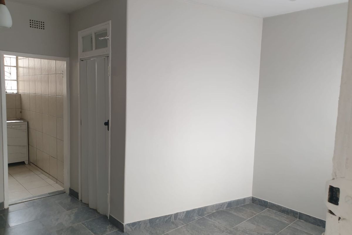 A bright, empty living area featuring neutral wall finishes and modern grey tiled flooring, with an adjacent view into a tiled utility or kitchen space.