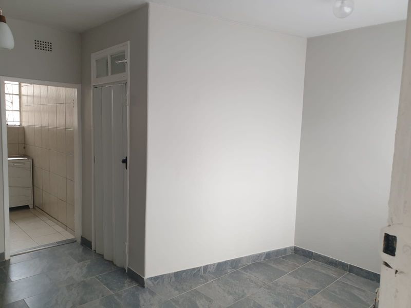 A bright, empty living area featuring neutral wall finishes and modern grey tiled flooring, with an adjacent view into a tiled utility or kitchen space.
