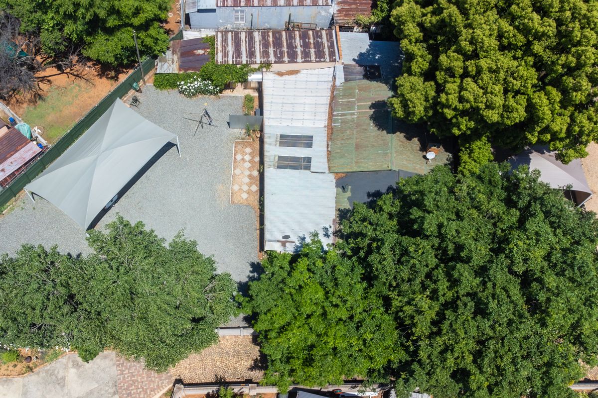 Aerial view of the property showing the main building with corrugated metal roofing, a gravel driveway, and a large shade sail structure.