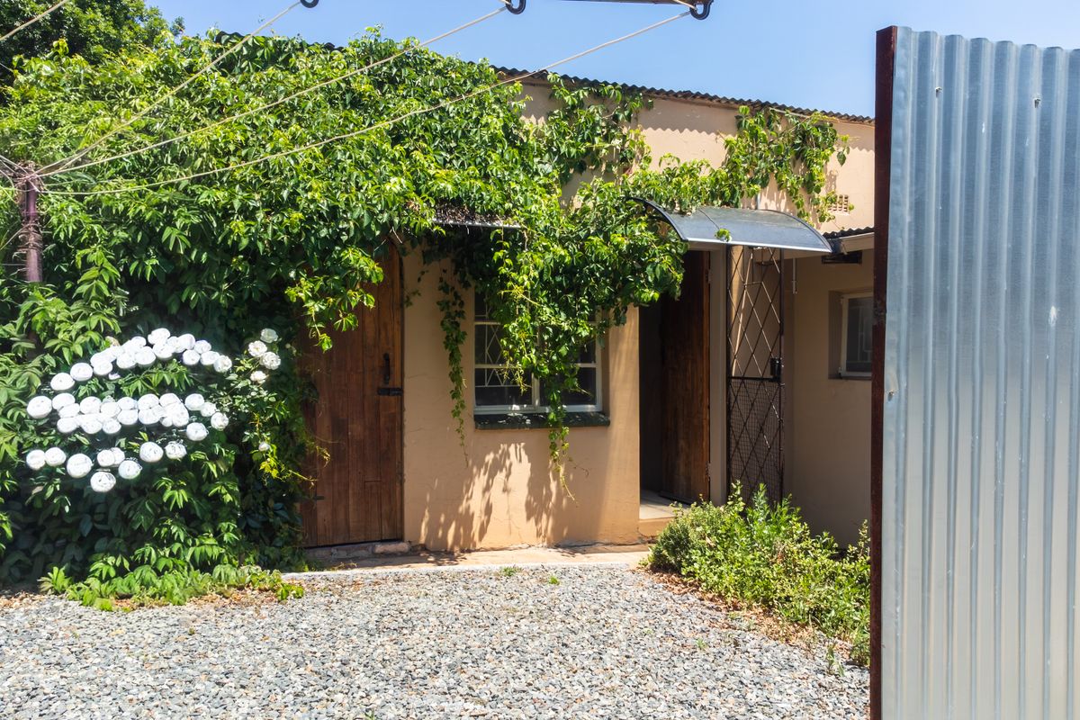 Rear exterior view of the property featuring timber doors, a metal awning, and a gravel area, partially obscured by overgrown climbing plants.