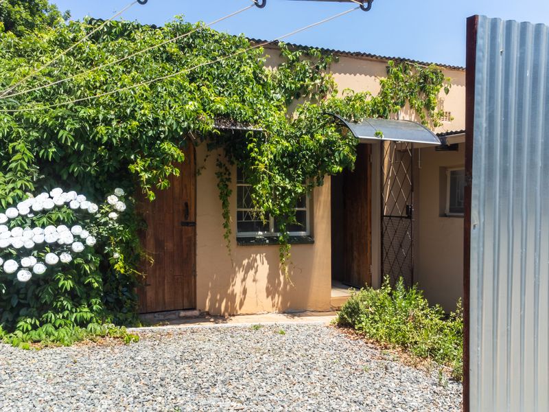 Rear exterior view of the property featuring timber doors, a metal awning, and a gravel area, partially obscured by overgrown climbing plants.