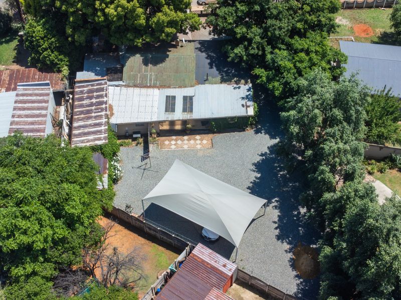 Aerial view of the property showing a large gravel driveway, shade sail carport, and multiple structures with corrugated metal roofing.