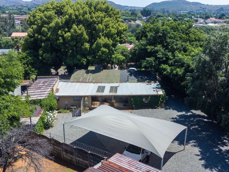 Aerial view of the property featuring a corrugated metal roof with solar panels, a gravel driveway, and a large shade sail carport.