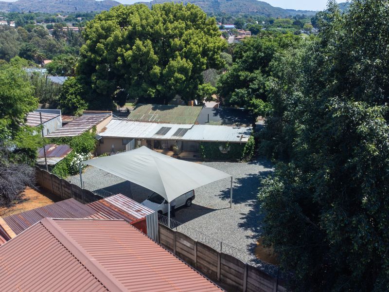 Aerial view of the property grounds featuring a gravel driveway, a large shade sail structure, and mature trees surrounding the main dwelling.