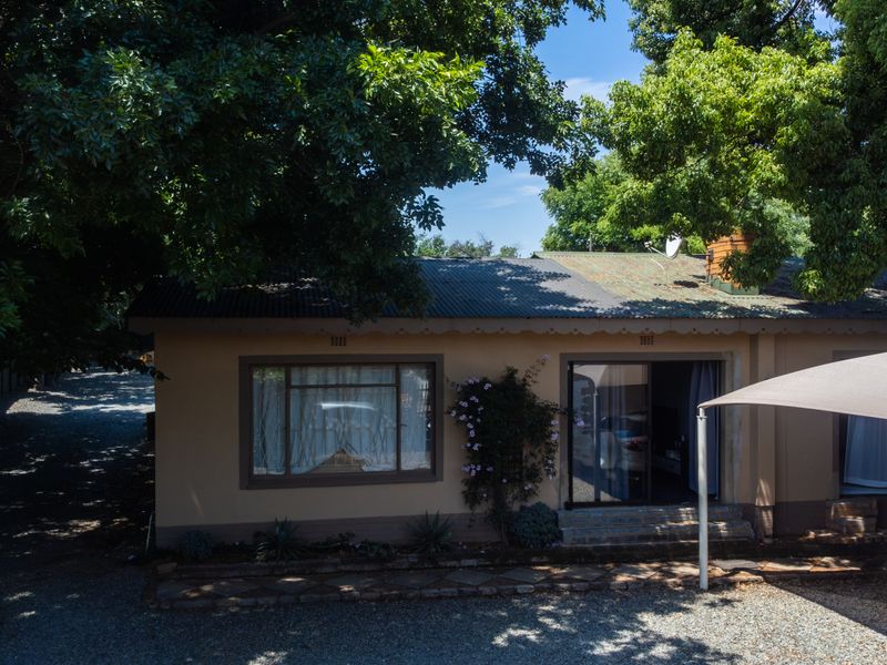 Rear view of the property featuring a corrugated metal roof, sliding glass door access, and a gravel driveway with a shade sail.