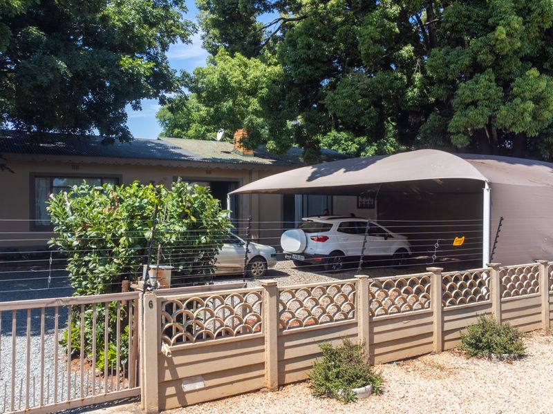 Front exterior view of the property featuring a gravel driveway, a covered carport, and secure boundary walling with electric fencing.