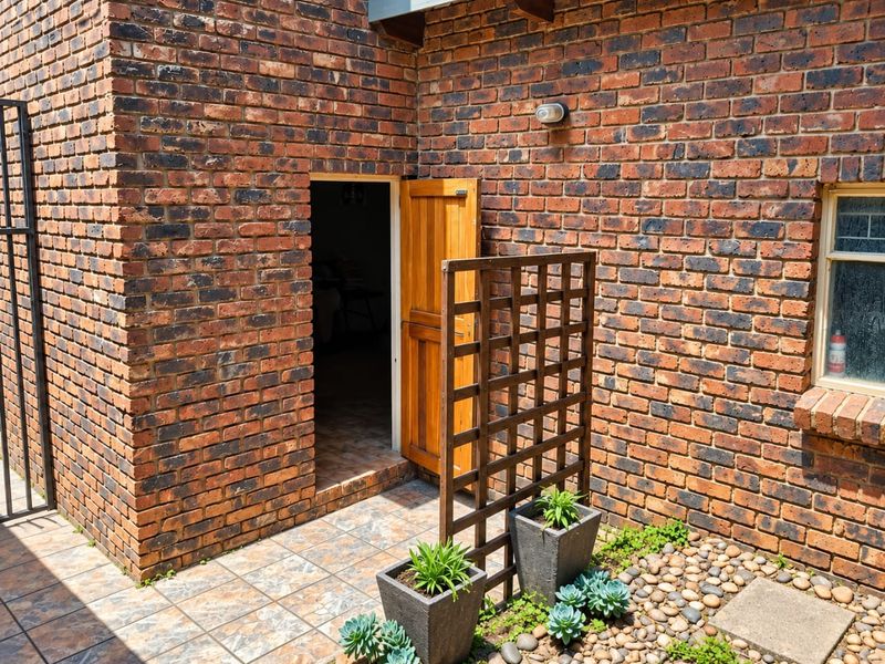 A rear exterior view featuring a face brick wall, tiled patio area, and a wooden door leading into the home.