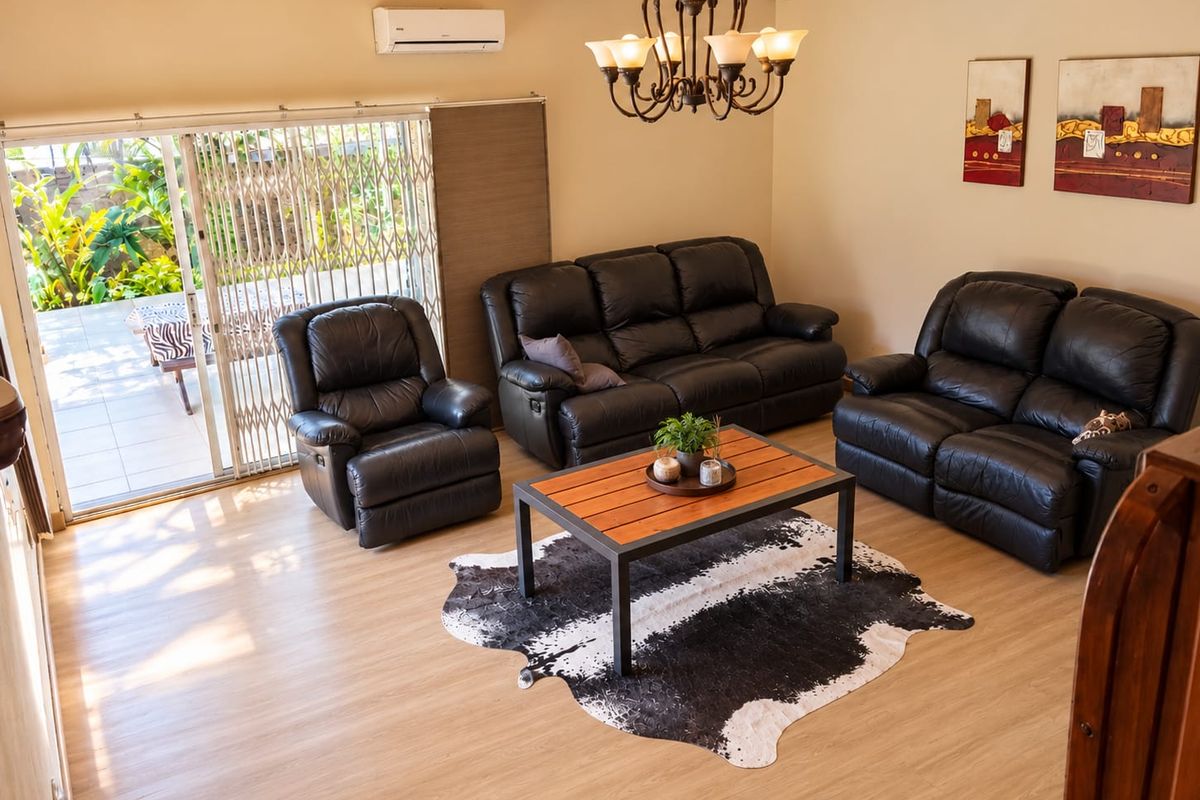Spacious living room featuring exposed timber ceiling beams, a split-system air conditioner, and large sliding glass doors providing direct access to the patio.