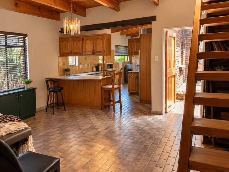 Open-plan kitchen and living area featuring exposed timber ceiling beams, tiled flooring, and a wooden staircase leading to an upper level.