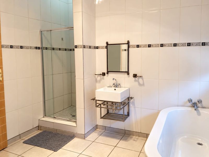 A clean, functional bathroom featuring a glass-enclosed shower, a modern wall-mounted basin, and a classic freestanding bathtub with white tiled finishes.