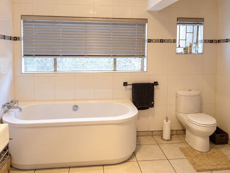 A clean and functional bathroom featuring a modern freestanding bathtub, a dual-flush toilet, and neutral ceramic tiling throughout.