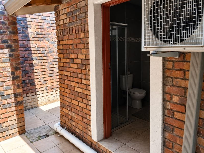 Exterior view showing a brick-walled bathroom entrance with tiled flooring and an external air conditioning unit mounted on the wall.