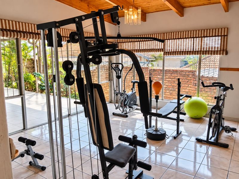 A bright home gym featuring exposed timber beams, ceramic tiled flooring, and large glass sliding doors providing ample natural light and garden views.