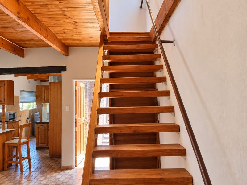 Open plan living area featuring a prominent wooden staircase, exposed timber ceiling beams, and tiled flooring, with an adjacent kitchen area.