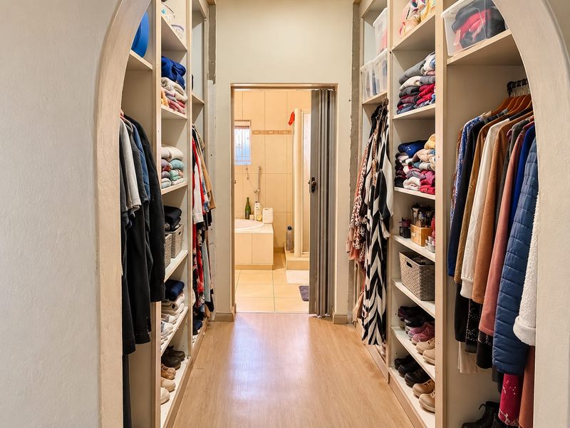 A walk-in closet area featuring extensive built-in shelving and hanging space, leading directly into an adjoining bathroom.