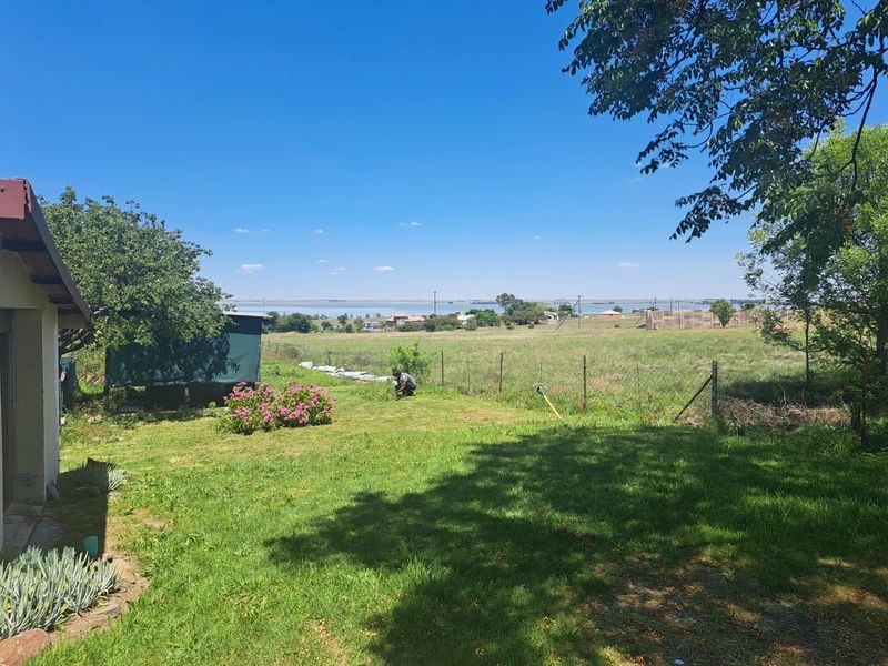 A spacious backyard garden featuring a well-maintained lawn, mature trees, and wire mesh fencing, offering an open outlook over the surrounding landscape.