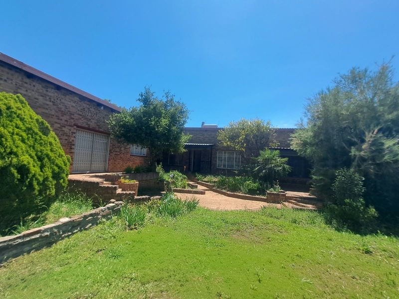 Rear view of a face brick house featuring a garden with paved pathways and established landscaping.