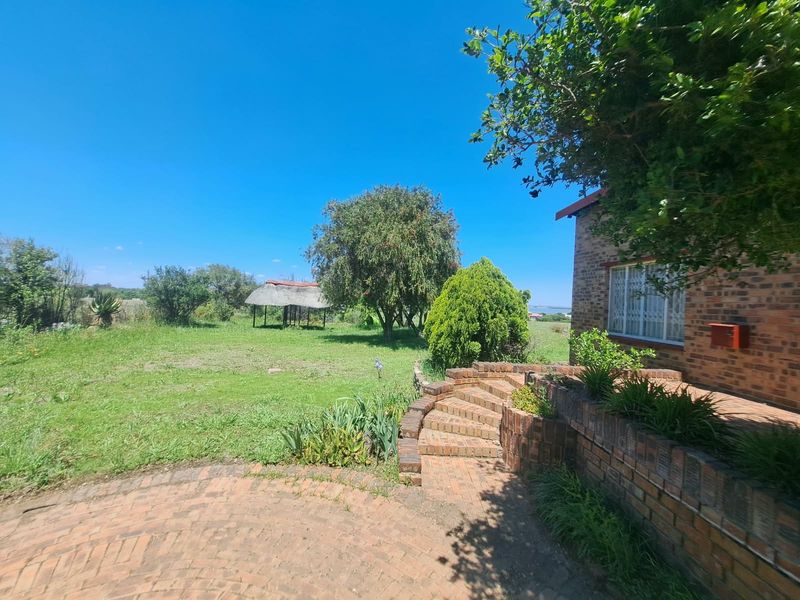 A spacious rear garden featuring a brick-paved patio, tiered brick steps, and a traditional thatched gazebo set within a large, open lawn area.