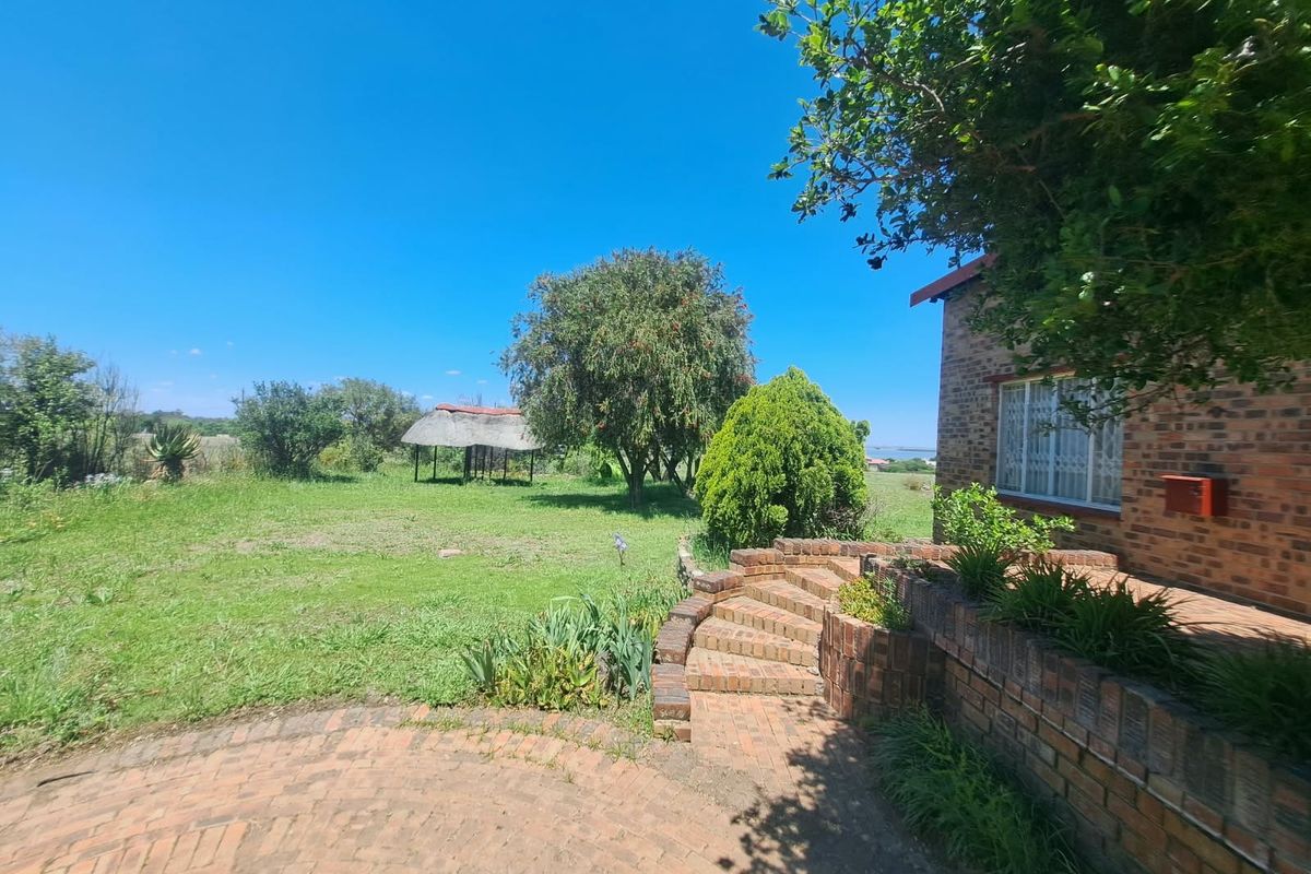 A spacious rear garden featuring a brick-paved patio, tiered brick steps, and a traditional thatched gazebo set within a large, open lawn area.