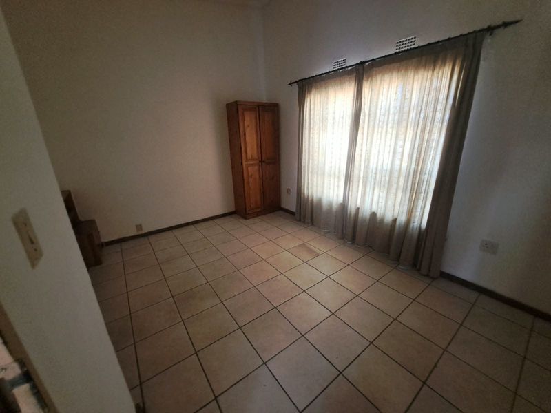 A vacant bedroom featuring tiled flooring and a large window with curtain rod, offering a blank canvas for potential interior design updates.