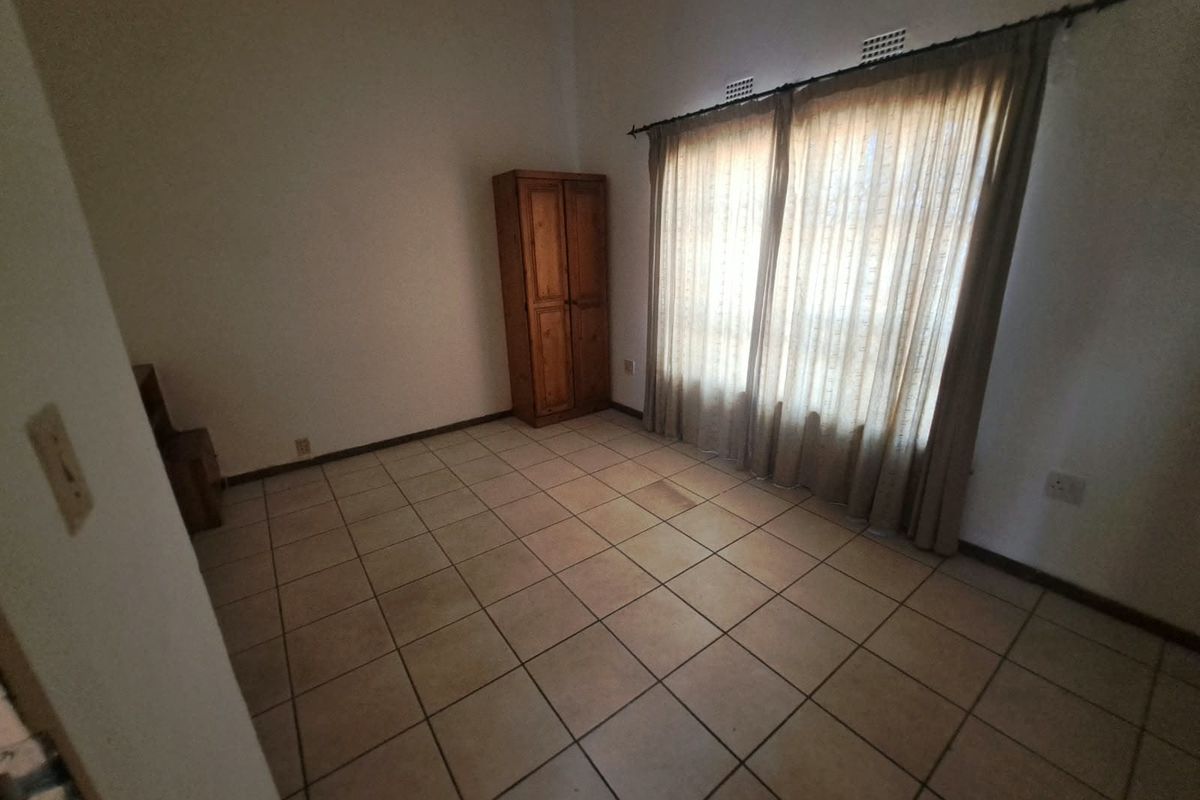 A vacant bedroom featuring tiled flooring and a large window with curtain rod, offering a blank canvas for potential interior design updates.